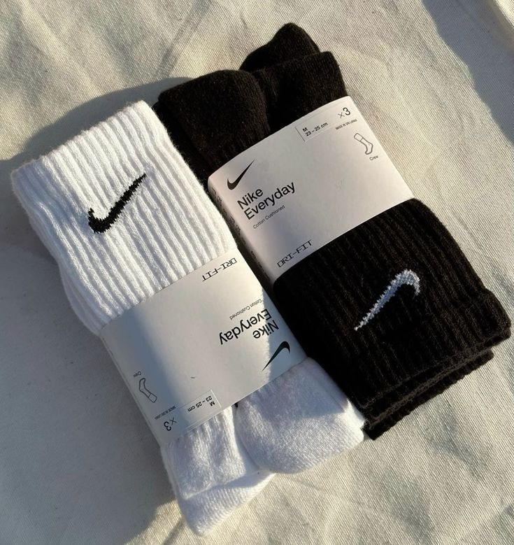 Two pairs of Nike socks, one white and one black, with packaging on a light gray background.